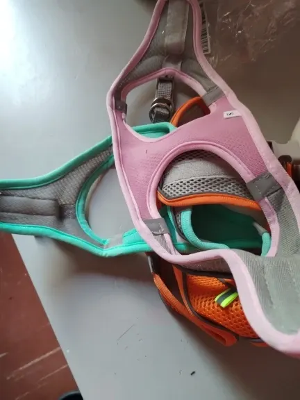 Pink, mint green and orange mesh cat harnesses stacked on a gray table, photographed by a verified buyer